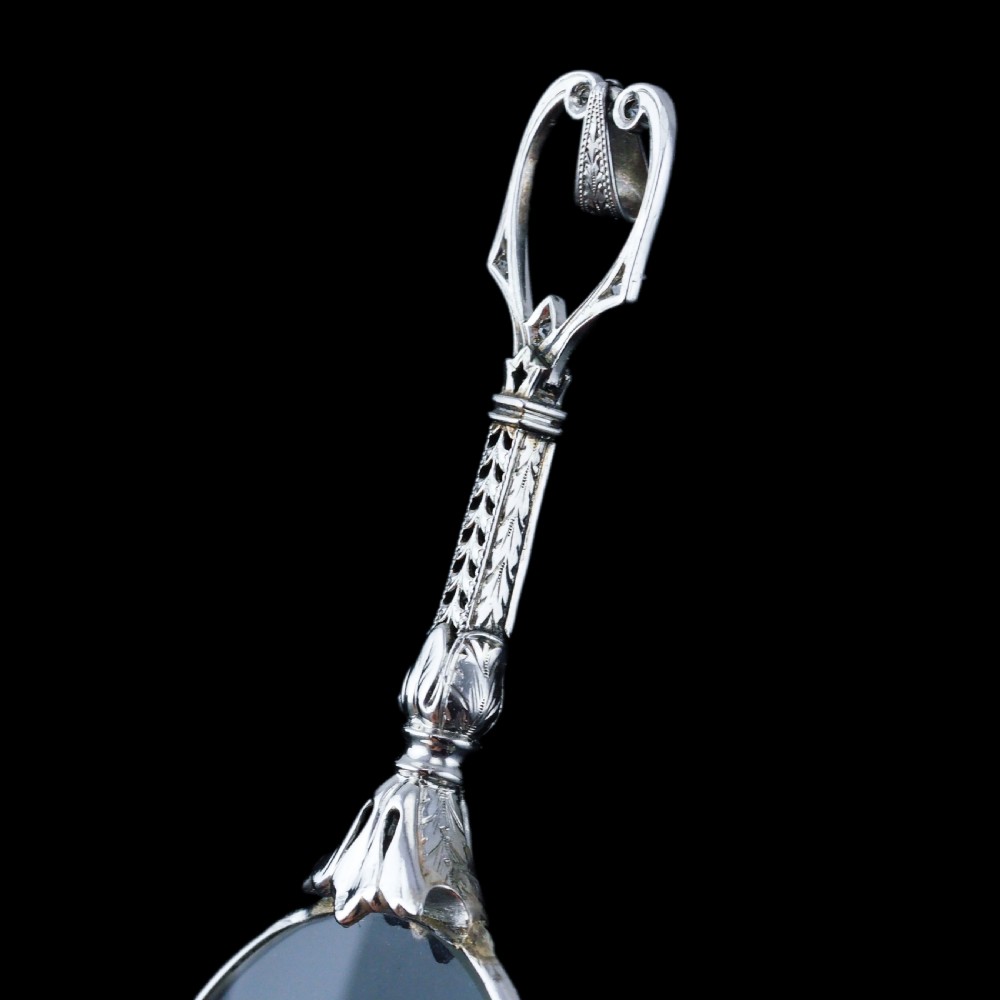 An Art Deco platinum lorgnette featuring a circular folding magnifying glass lens attached to a geometric handle set with small diamonds. View XXV