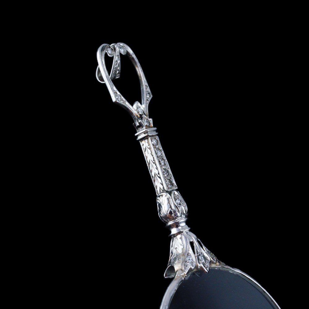 An Art Deco platinum lorgnette featuring a circular folding magnifying glass lens attached to a geometric handle set with small diamonds. View XXVI