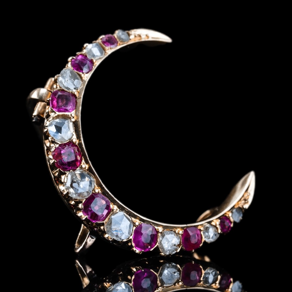An 18K gold Victorian crescent moon brooch set with alternating cushion-cut rubies and old-cut diamonds.