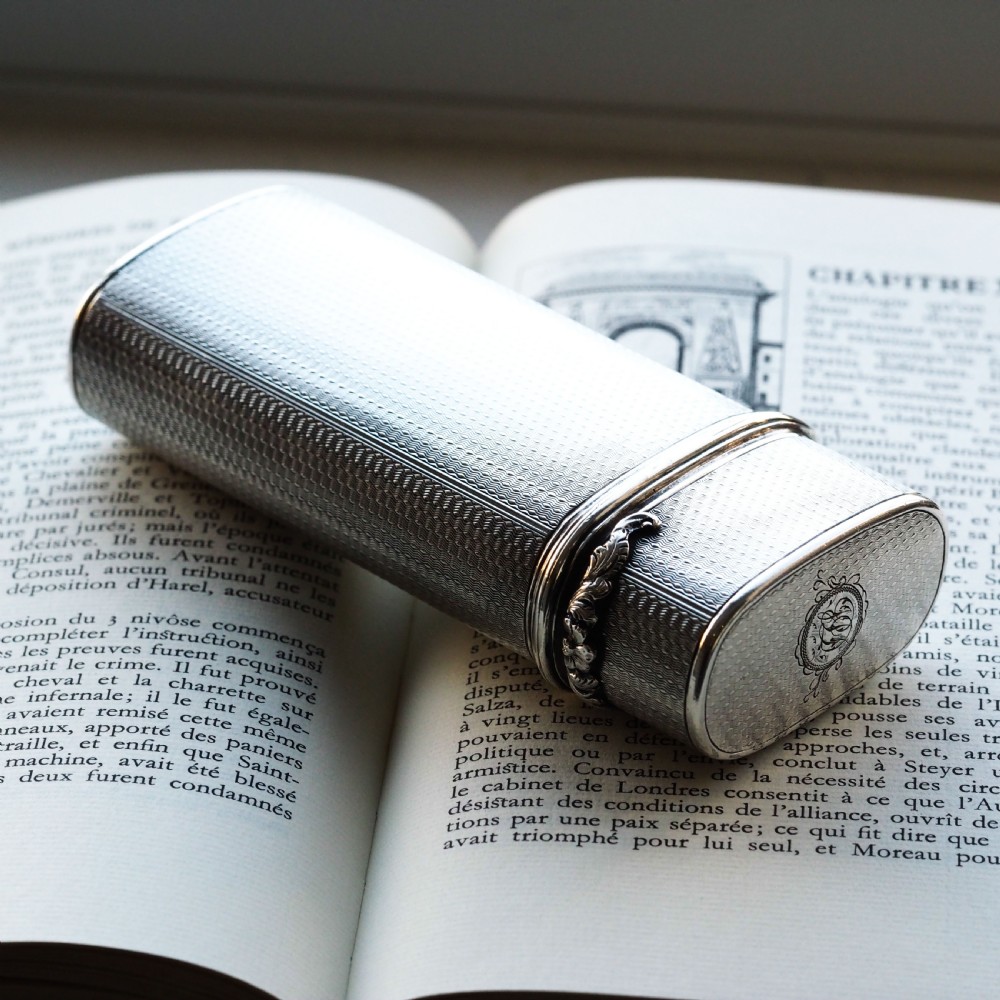 An antique engine-turned solid silver cigar case featuring floral relief thumbpiece detailing and an engraved cartouche on the end.