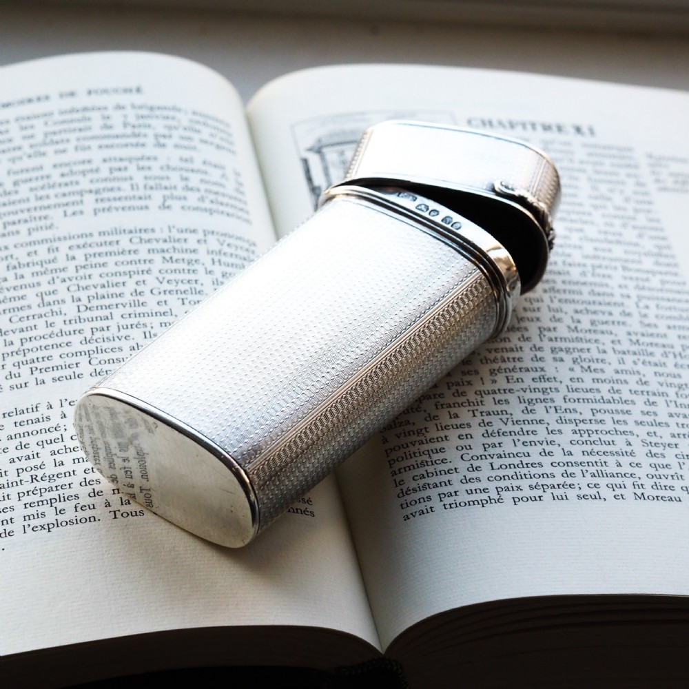 An antique engine-turned solid silver cigar case featuring floral relief thumbpiece detailing and an engraved cartouche on the end. View III