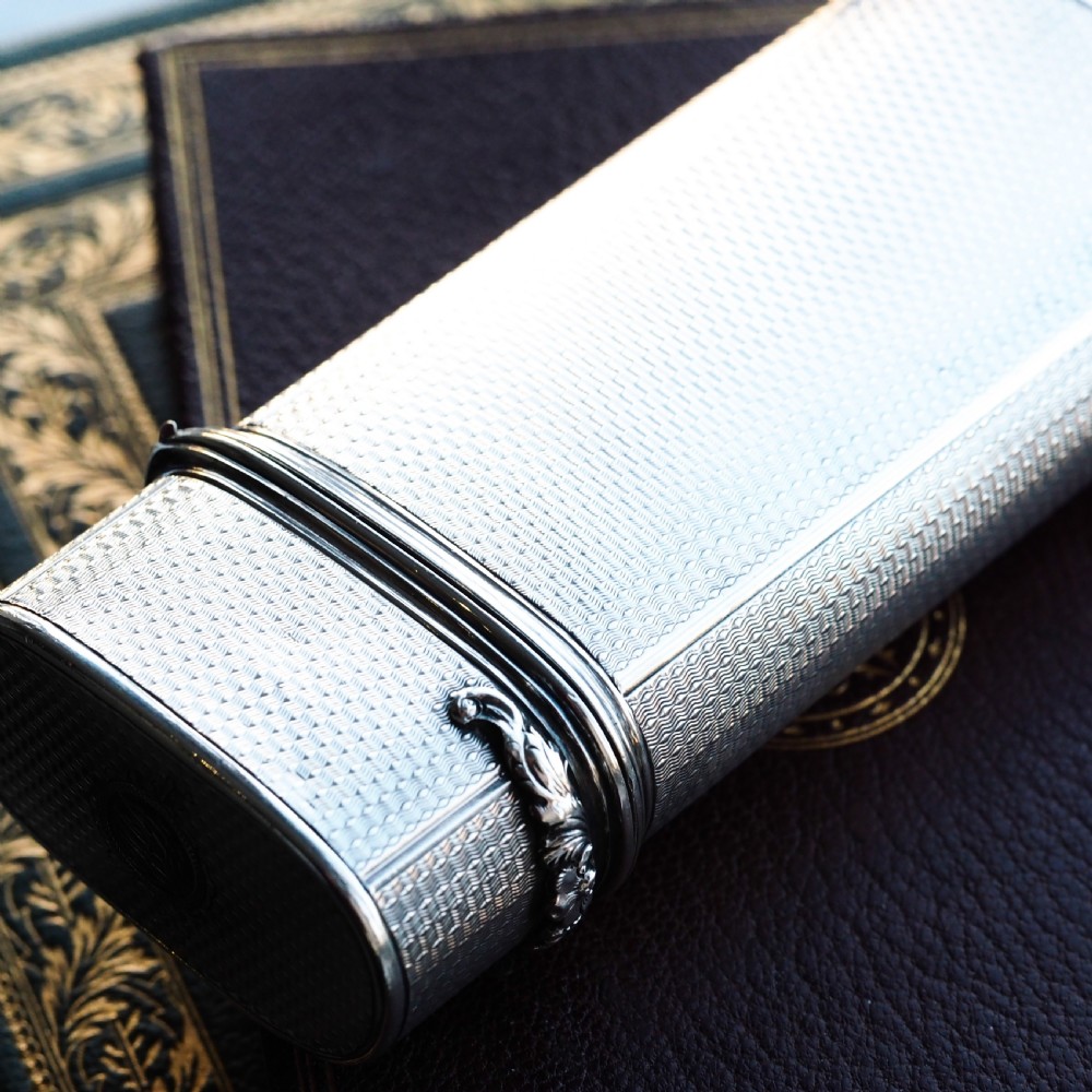 An antique engine-turned solid silver cigar case featuring floral relief thumbpiece detailing and an engraved cartouche on the end. View VI