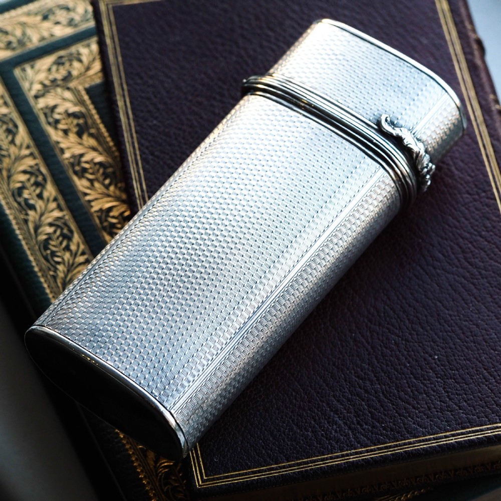 An antique engine-turned solid silver cigar case featuring floral relief thumbpiece detailing and an engraved cartouche on the end. View VII