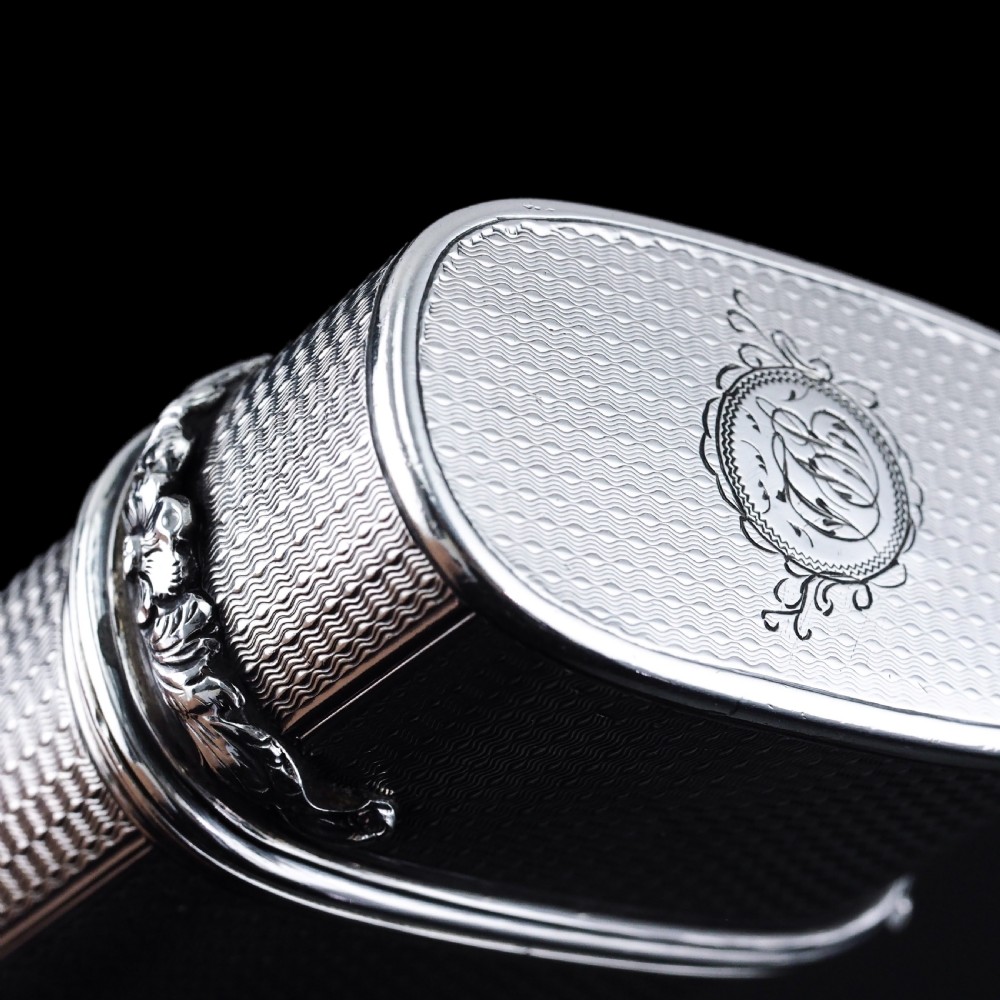 An antique engine-turned solid silver cigar case featuring floral relief thumbpiece detailing and an engraved cartouche on the end. View XIII