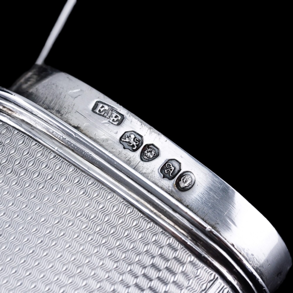An antique engine-turned solid silver cigar case featuring floral relief thumbpiece detailing and an engraved cartouche on the end. View XVII