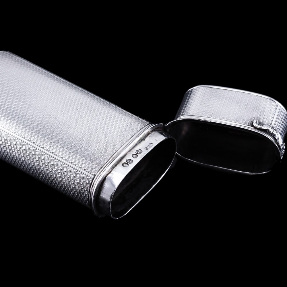 An antique engine-turned solid silver cigar case featuring floral relief thumbpiece detailing and an engraved cartouche on the end. View XVIII