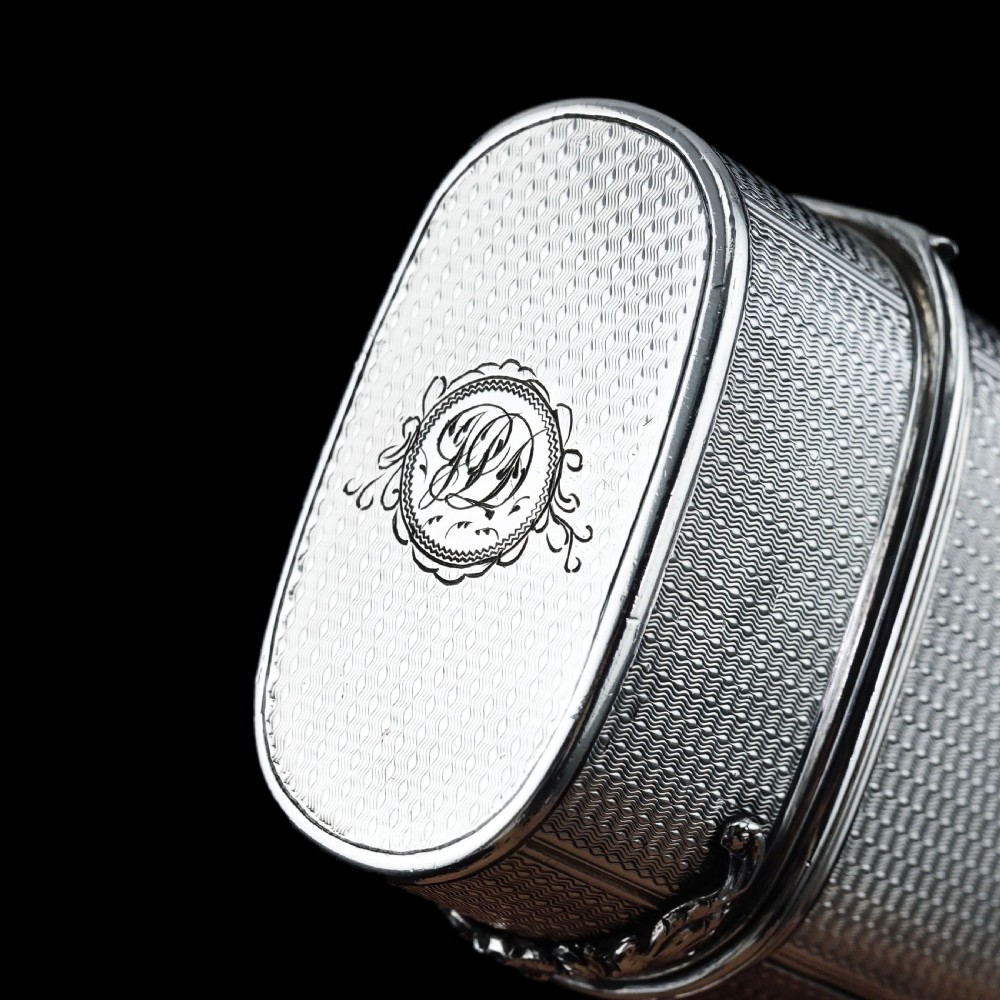 An antique engine-turned solid silver cigar case featuring floral relief thumbpiece detailing and an engraved cartouche on the end. View XIX