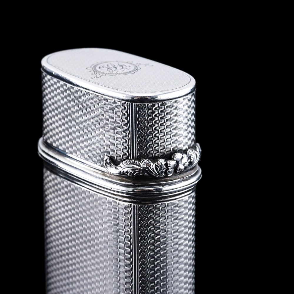 An antique engine-turned solid silver cigar case featuring floral relief thumbpiece detailing and an engraved cartouche on the end. View XXI