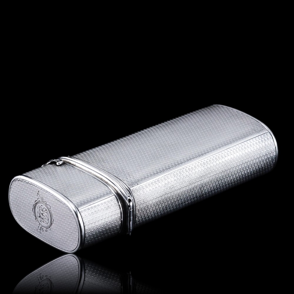 An antique engine-turned solid silver cigar case featuring floral relief thumbpiece detailing and an engraved cartouche on the end. View XXIV