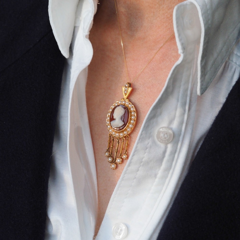 A Victorian 14K gold oval pendant featuring a carved white shell cameo profile against a brown background, framed by a border of seed pearls with articulated pearl drops. View V