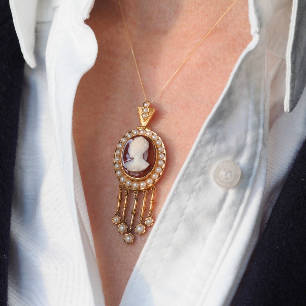 A Victorian 14K gold oval pendant featuring a carved white shell cameo profile against a brown background, framed by a border of seed pearls with articulated pearl drops. View VI