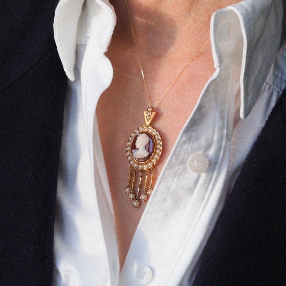 A Victorian 14K gold oval pendant featuring a carved white shell cameo profile against a brown background, framed by a border of seed pearls with articulated pearl drops. View VII