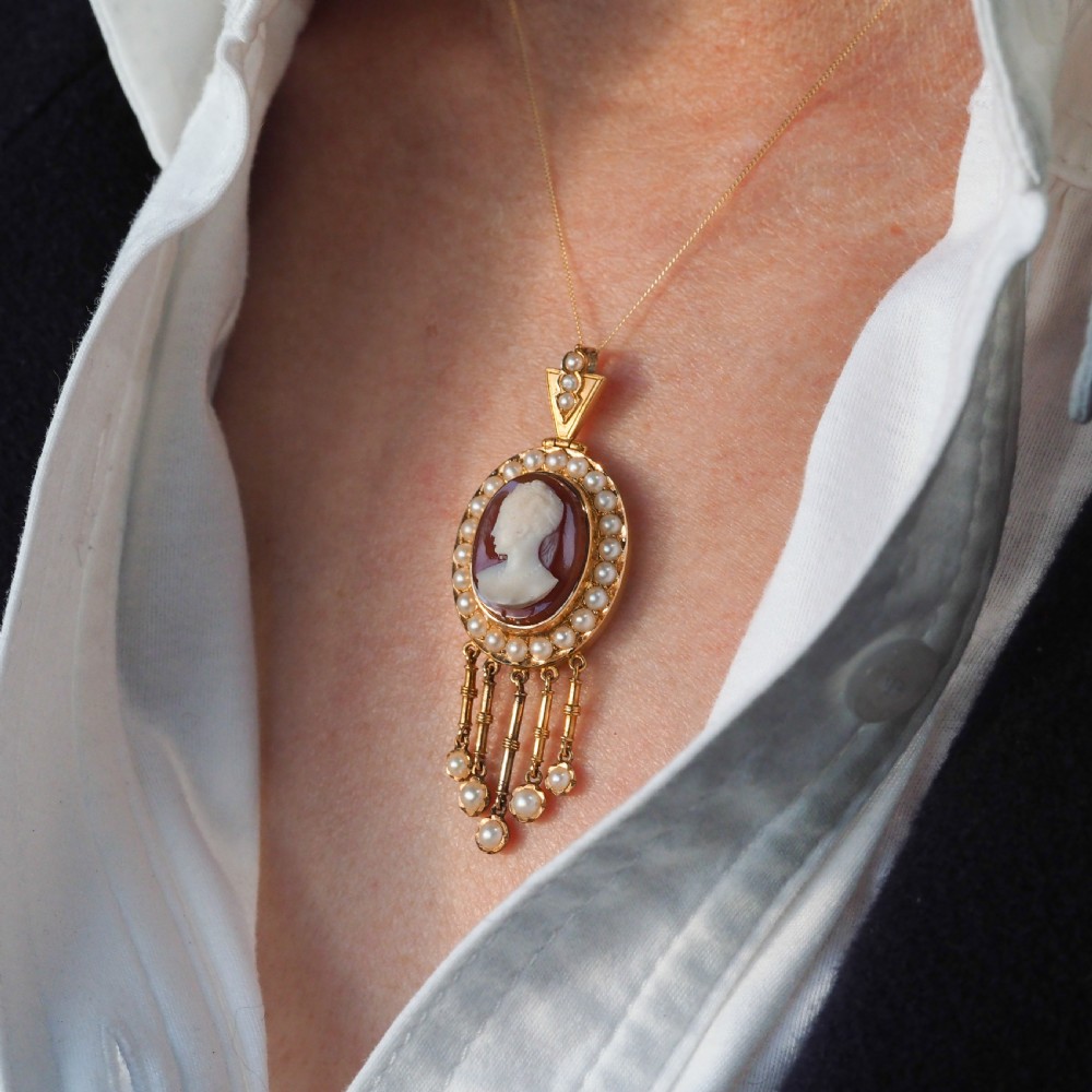 A Victorian 14K gold oval pendant featuring a carved white shell cameo profile against a brown background, framed by a border of seed pearls with articulated pearl drops. View IX