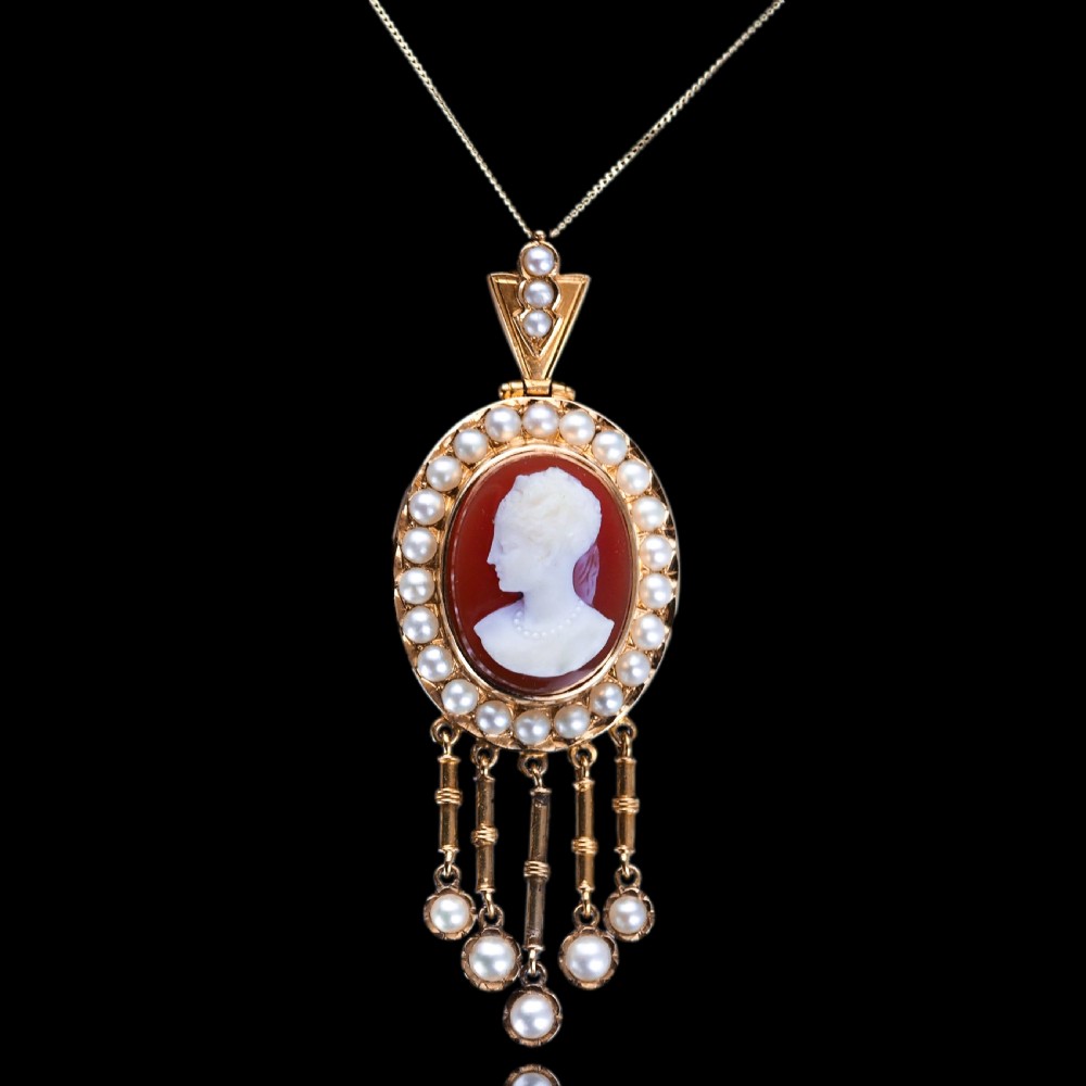 A Victorian 14K gold oval pendant featuring a carved white shell cameo profile against a brown background, framed by a border of seed pearls with articulated pearl drops. View XII