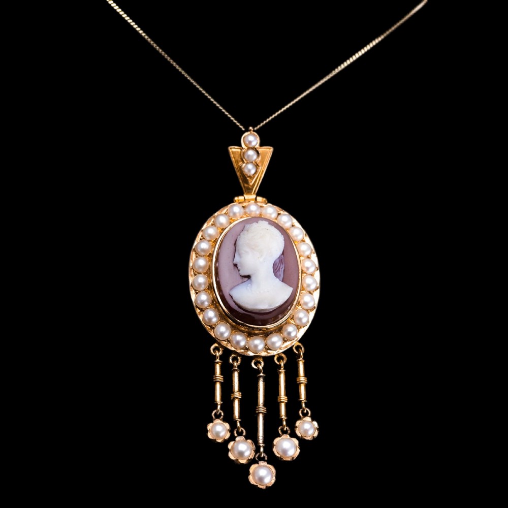 A Victorian 14K gold oval pendant featuring a carved white shell cameo profile against a brown background, framed by a border of seed pearls with articulated pearl drops. View XV