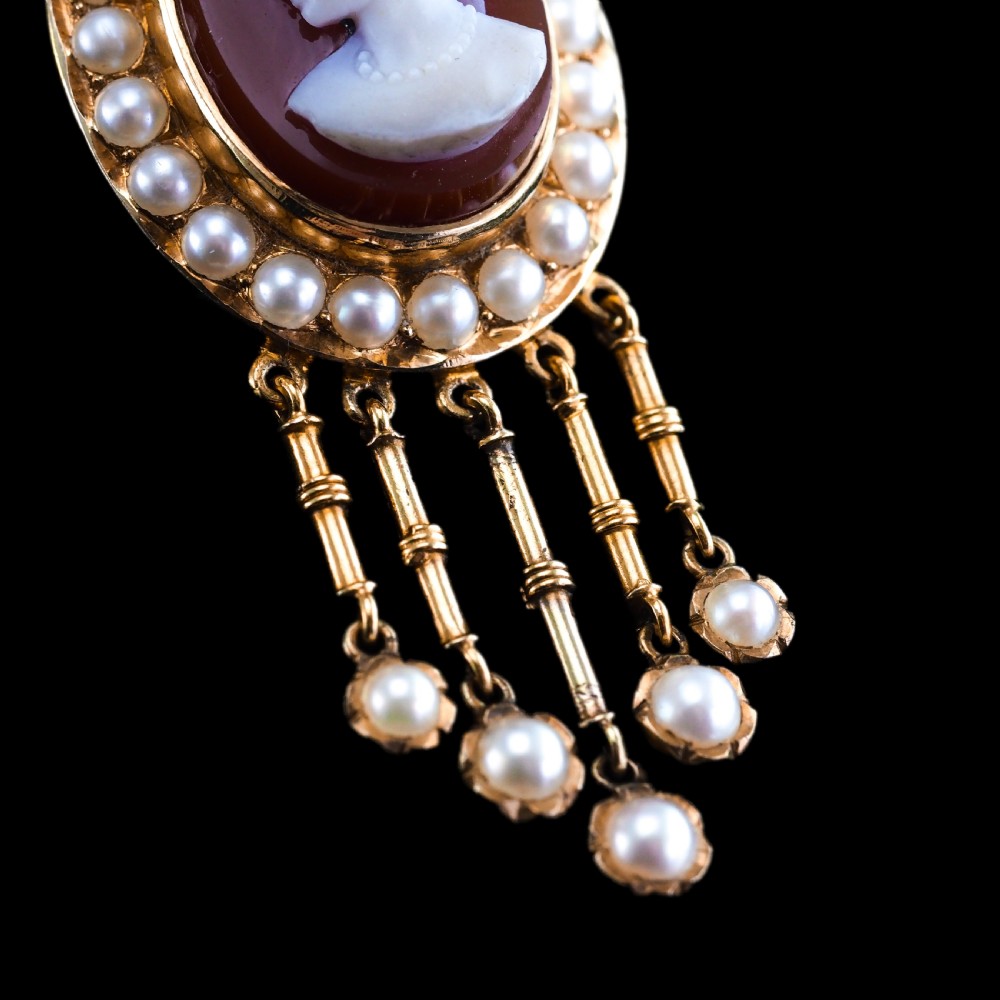 A Victorian 14K gold oval pendant featuring a carved white shell cameo profile against a brown background, framed by a border of seed pearls with articulated pearl drops. View XVI