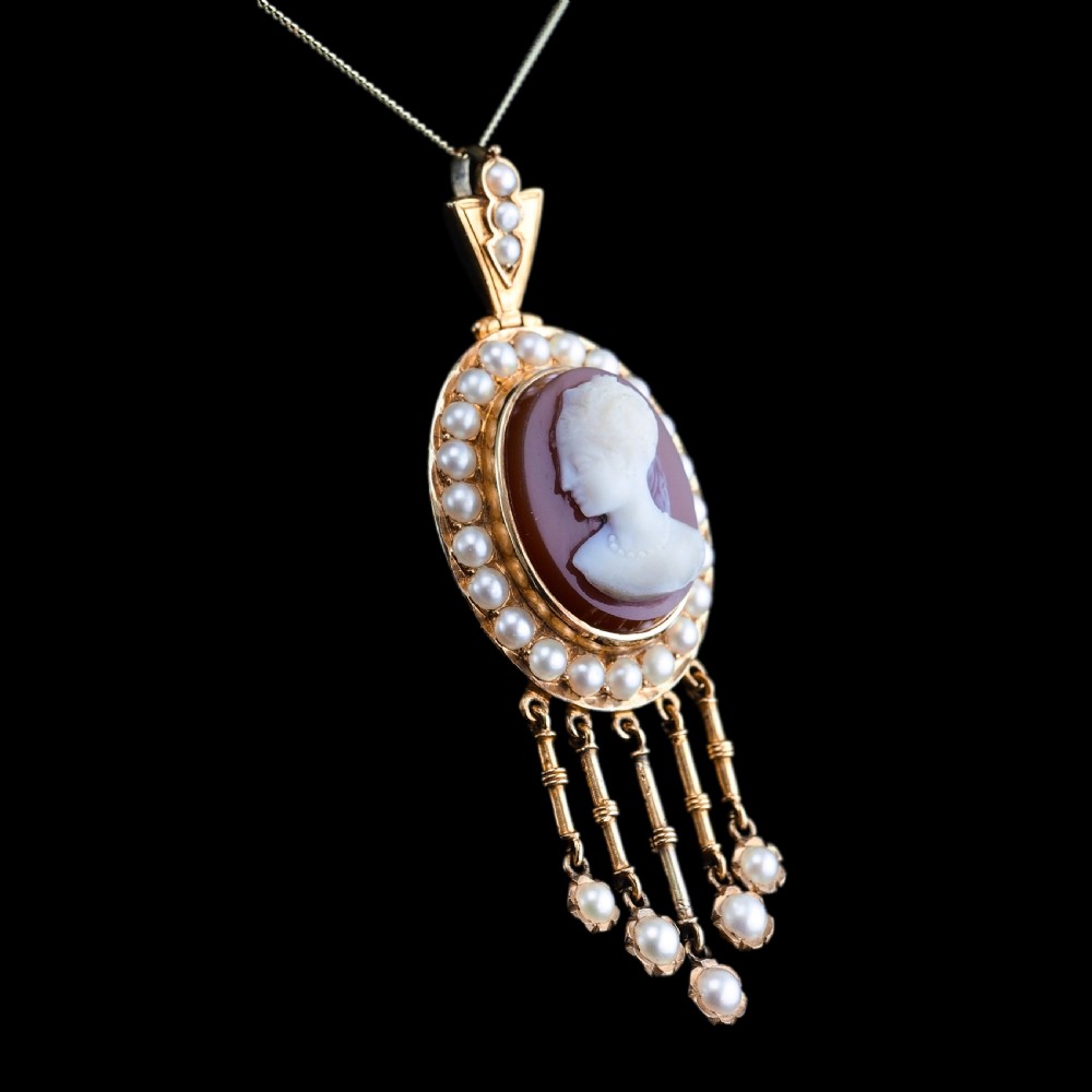 A Victorian 14K gold oval pendant featuring a carved white shell cameo profile against a brown background, framed by a border of seed pearls with articulated pearl drops. View XVII