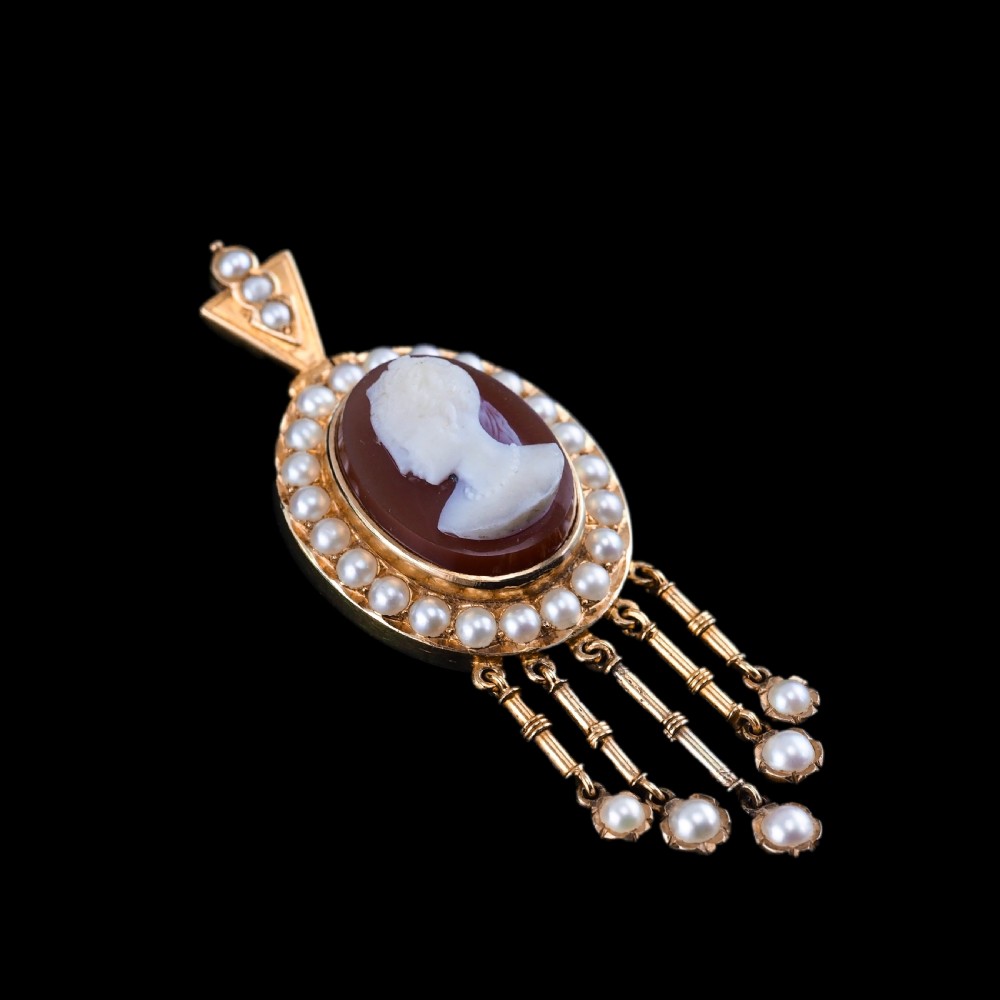A Victorian 14K gold oval pendant featuring a carved white shell cameo profile against a brown background, framed by a border of seed pearls with articulated pearl drops. View XIX