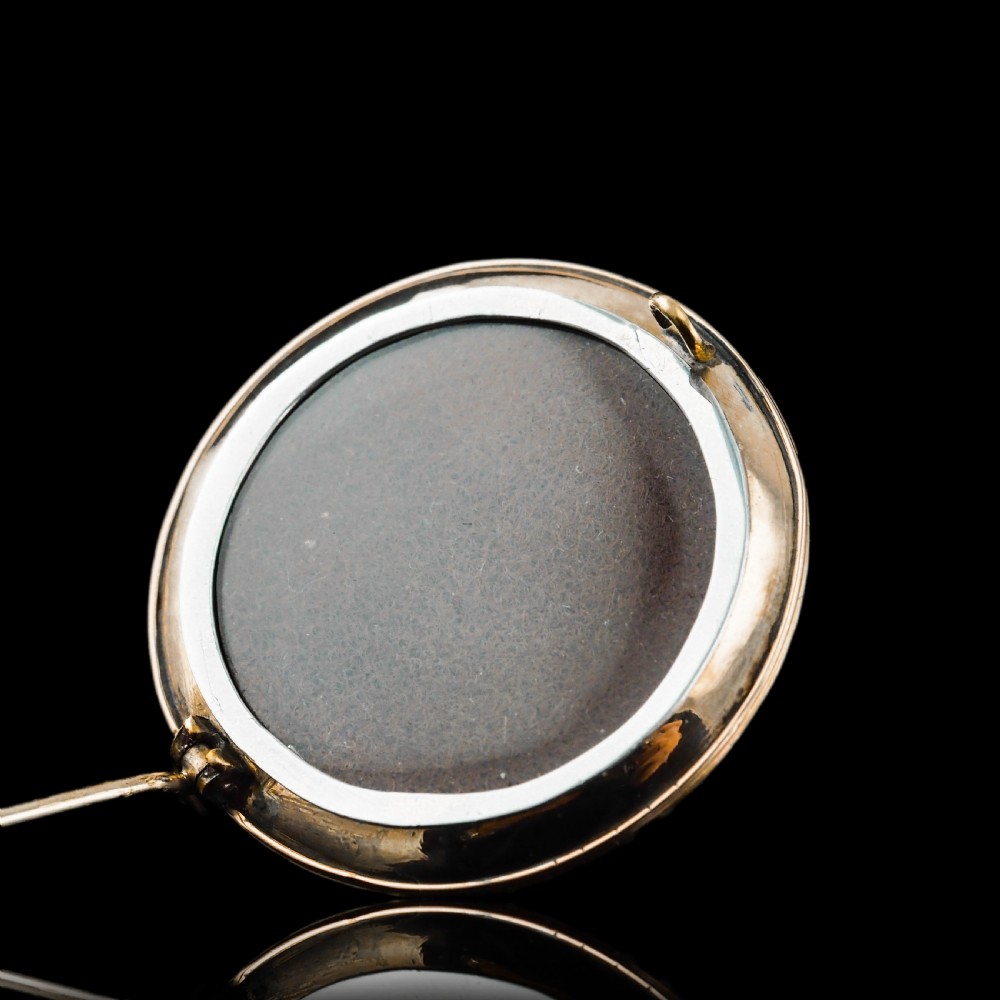 A circular Victorian red guilloche enamel brooch featuring concentric seed pearl borders, a central dark garnet cabochon, and a small turquoise accent set in gold. View XII