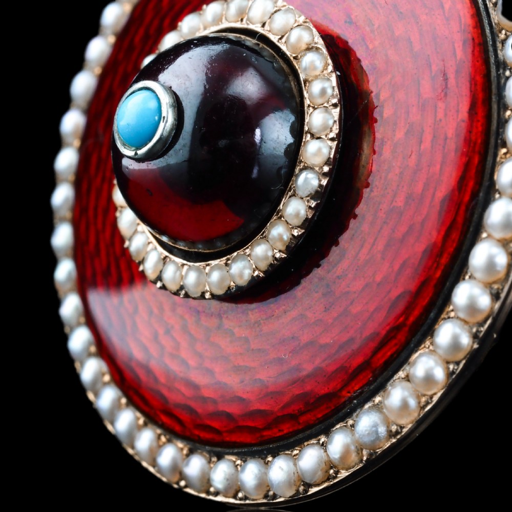 A circular Victorian red guilloche enamel brooch featuring concentric seed pearl borders, a central dark garnet cabochon, and a small turquoise accent set in gold. View XIII