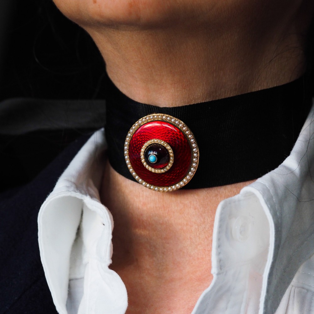A circular Victorian red guilloche enamel brooch featuring concentric seed pearl borders, a central dark garnet cabochon, and a small turquoise accent set in gold. View XIV