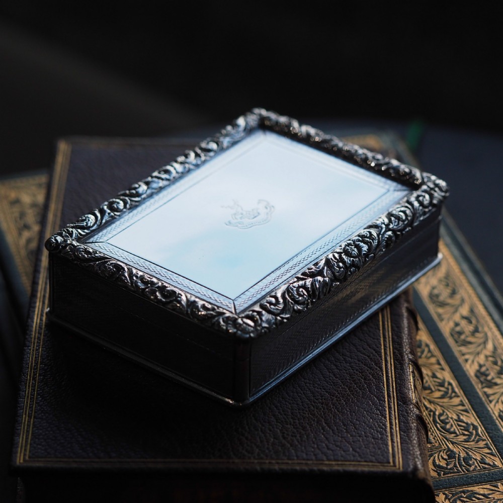 A rectangular sterling silver table snuff box featuring a chased floral border, an engine-turned cover with a central engraved crest, and straight sides.