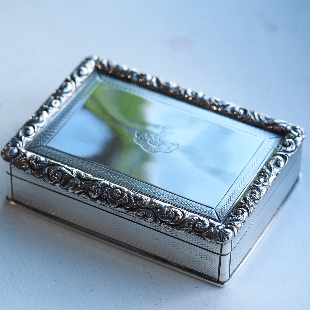 A rectangular sterling silver table snuff box featuring a chased floral border, an engine-turned cover with a central engraved crest, and straight sides. View V
