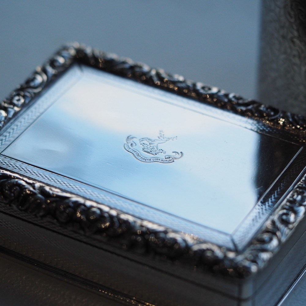 A rectangular sterling silver table snuff box featuring a chased floral border, an engine-turned cover with a central engraved crest, and straight sides. View XXI