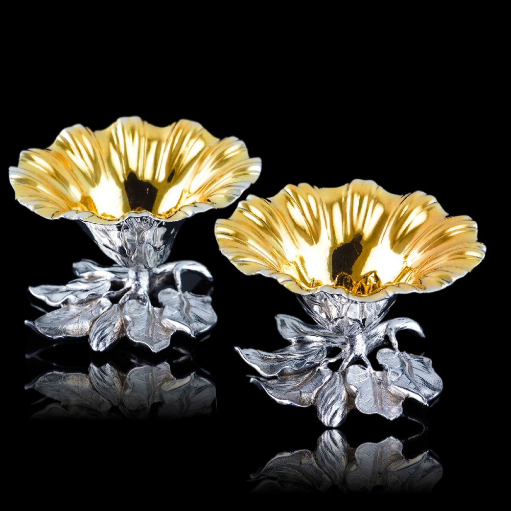 A pair of William IV sterling silver salt cellars designed as open flower heads with gilded interiors resting on naturalistic leaf bases.