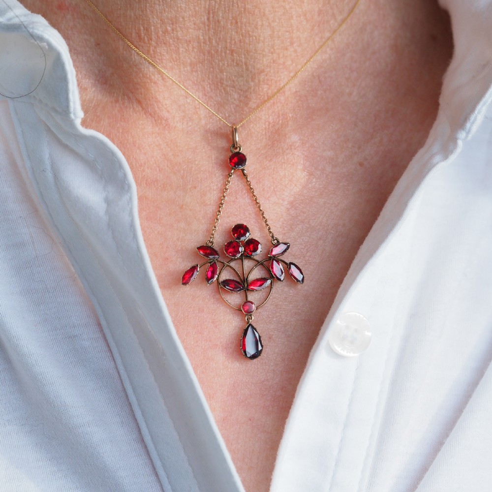 An Art Nouveau 9ct gold pendant necklace featuring marquise and round cut deep red garnets arranged in a foliate motif with a teardrop drop stone. View IV