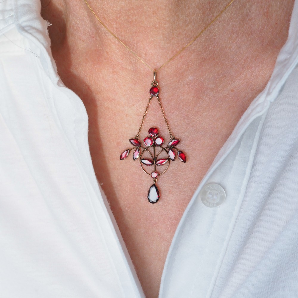 An Art Nouveau 9ct gold pendant necklace featuring marquise and round cut deep red garnets arranged in a foliate motif with a teardrop drop stone. View V