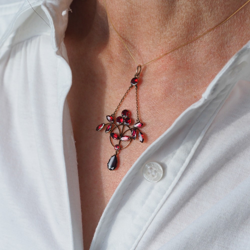 An Art Nouveau 9ct gold pendant necklace featuring marquise and round cut deep red garnets arranged in a foliate motif with a teardrop drop stone. View VI