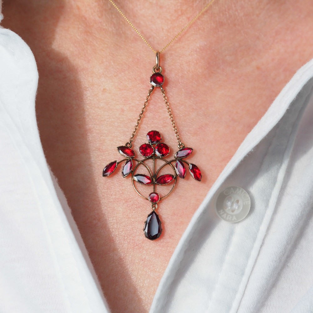An Art Nouveau 9ct gold pendant necklace featuring marquise and round cut deep red garnets arranged in a foliate motif with a teardrop drop stone. View VII
