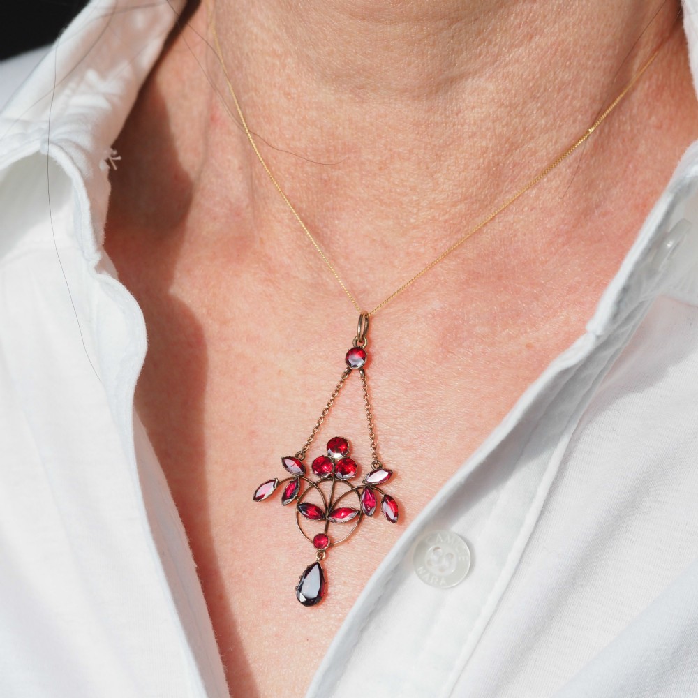 An Art Nouveau 9ct gold pendant necklace featuring marquise and round cut deep red garnets arranged in a foliate motif with a teardrop drop stone. View IX