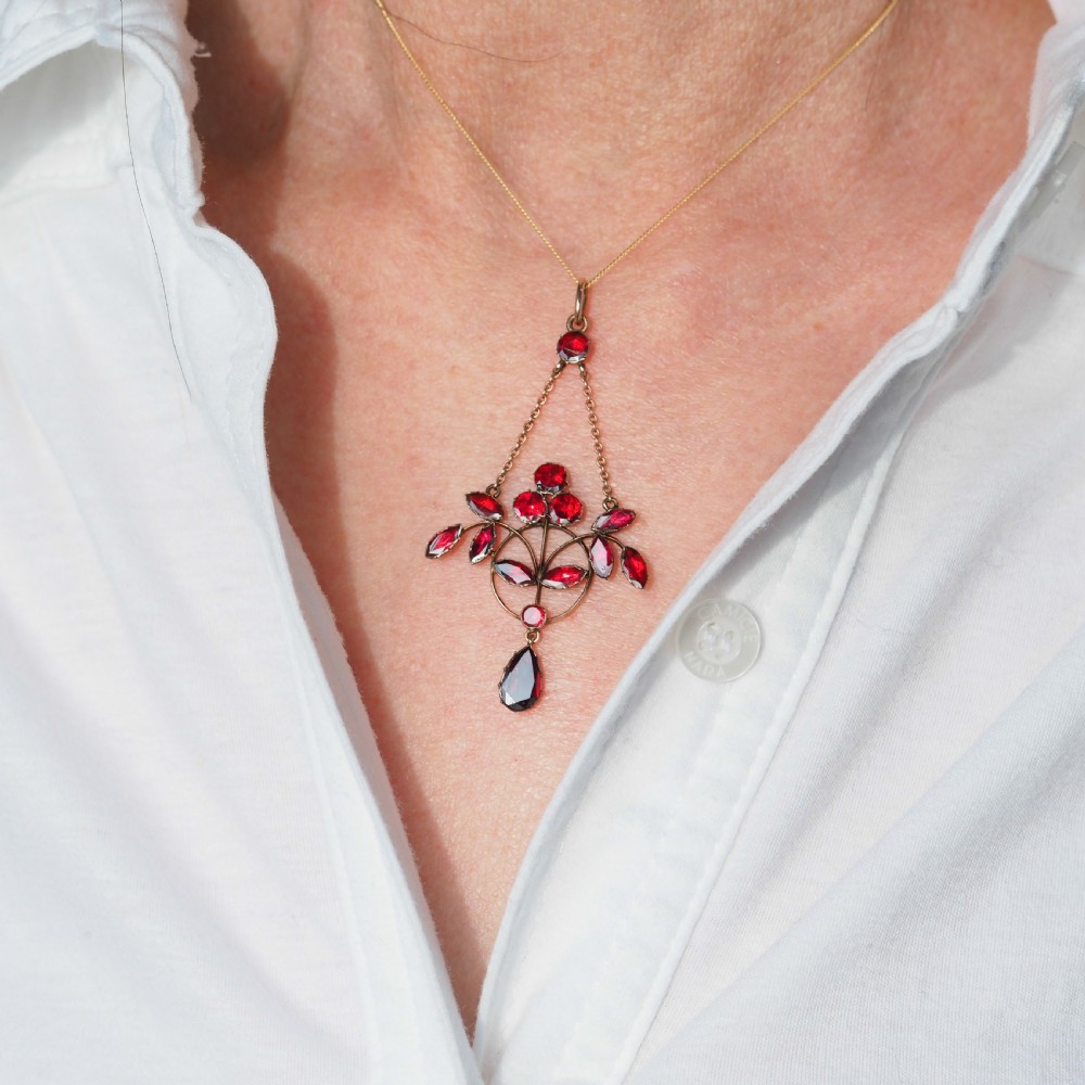 An Art Nouveau 9ct gold pendant necklace featuring marquise and round cut deep red garnets arranged in a foliate motif with a teardrop drop stone. View X