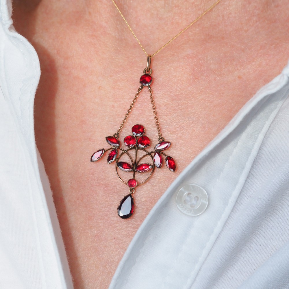 An Art Nouveau 9ct gold pendant necklace featuring marquise and round cut deep red garnets arranged in a foliate motif with a teardrop drop stone. View XI