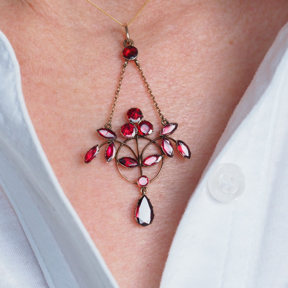 An Art Nouveau 9ct gold pendant necklace featuring marquise and round cut deep red garnets arranged in a foliate motif with a teardrop drop stone. View XII