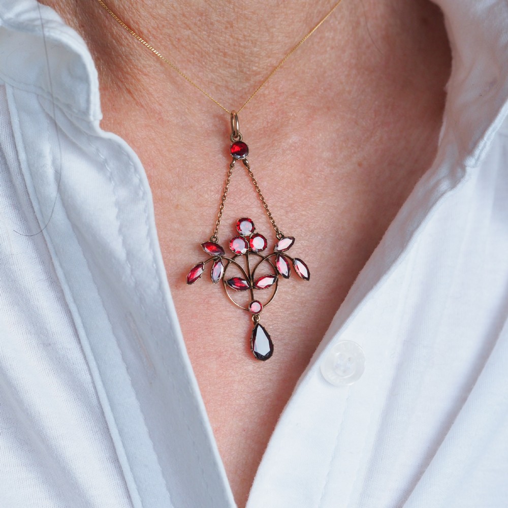 An Art Nouveau 9ct gold pendant necklace featuring marquise and round cut deep red garnets arranged in a foliate motif with a teardrop drop stone. View XIII