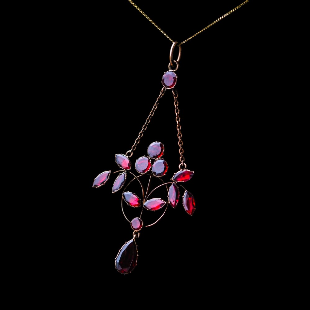 An Art Nouveau 9ct gold pendant necklace featuring marquise and round cut deep red garnets arranged in a foliate motif with a teardrop drop stone. View XIV