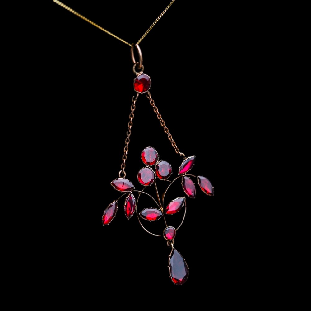 An Art Nouveau 9ct gold pendant necklace featuring marquise and round cut deep red garnets arranged in a foliate motif with a teardrop drop stone. View XV