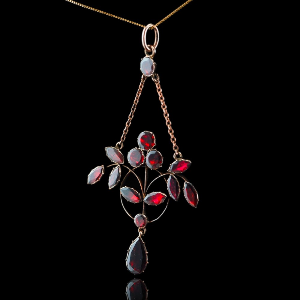 An Art Nouveau 9ct gold pendant necklace featuring marquise and round cut deep red garnets arranged in a foliate motif with a teardrop drop stone. View XVI
