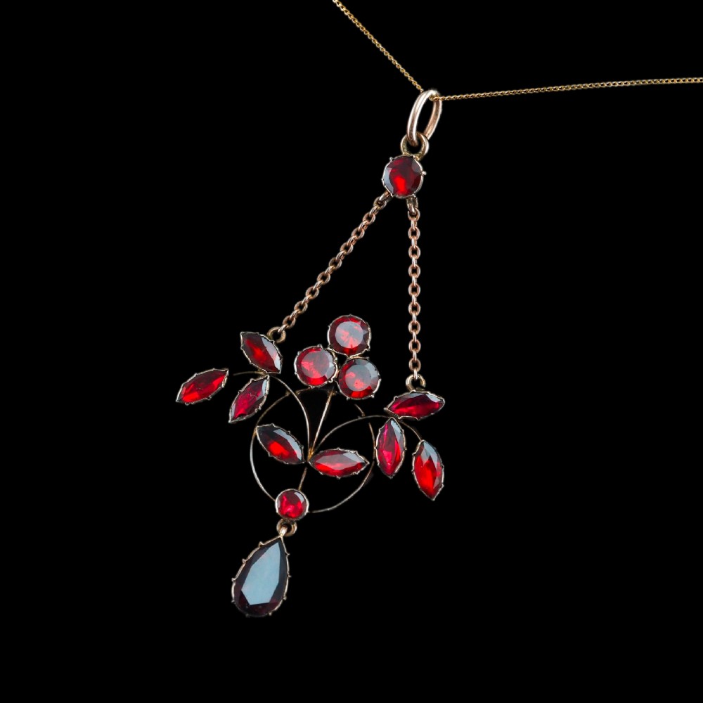An Art Nouveau 9ct gold pendant necklace featuring marquise and round cut deep red garnets arranged in a foliate motif with a teardrop drop stone. View XVIII