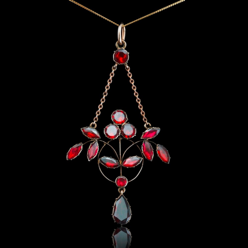 An Art Nouveau 9ct gold pendant necklace featuring marquise and round cut deep red garnets arranged in a foliate motif with a teardrop drop stone. View XIX