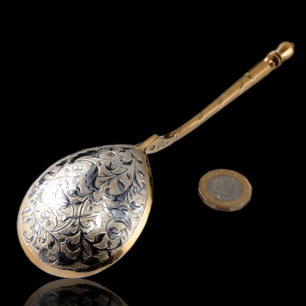 An antique Russian silver-gilt serving spoon featuring intricate black niello foliate engraving across the back of the oval bowl and a turned stem.