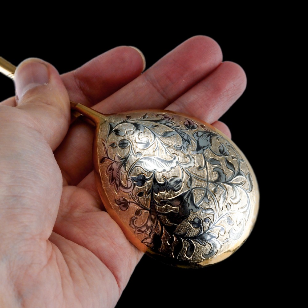 An antique Russian silver-gilt serving spoon featuring intricate black niello foliate engraving across the back of the oval bowl and a turned stem. View VI