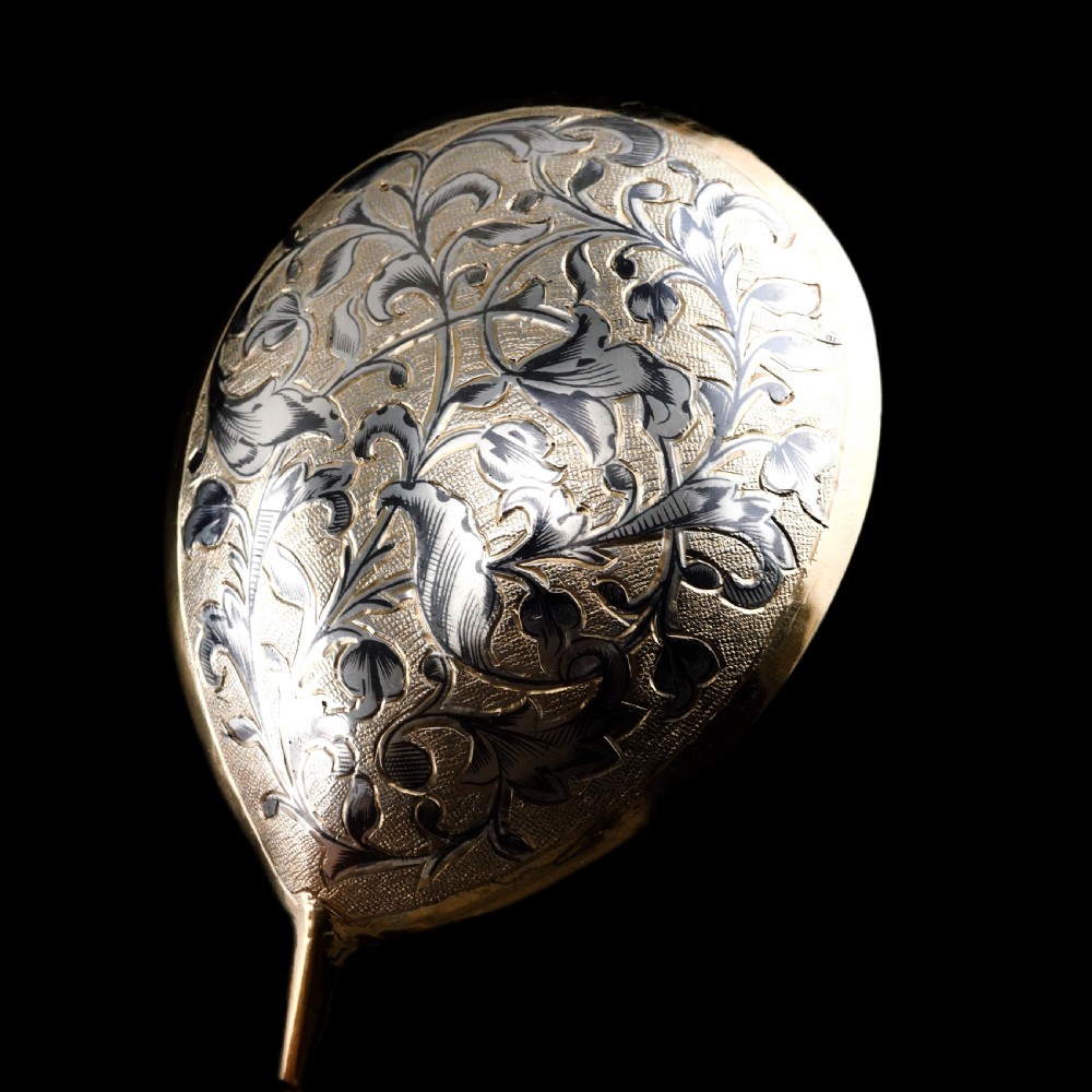 An antique Russian silver-gilt serving spoon featuring intricate black niello foliate engraving across the back of the oval bowl and a turned stem. View XVI
