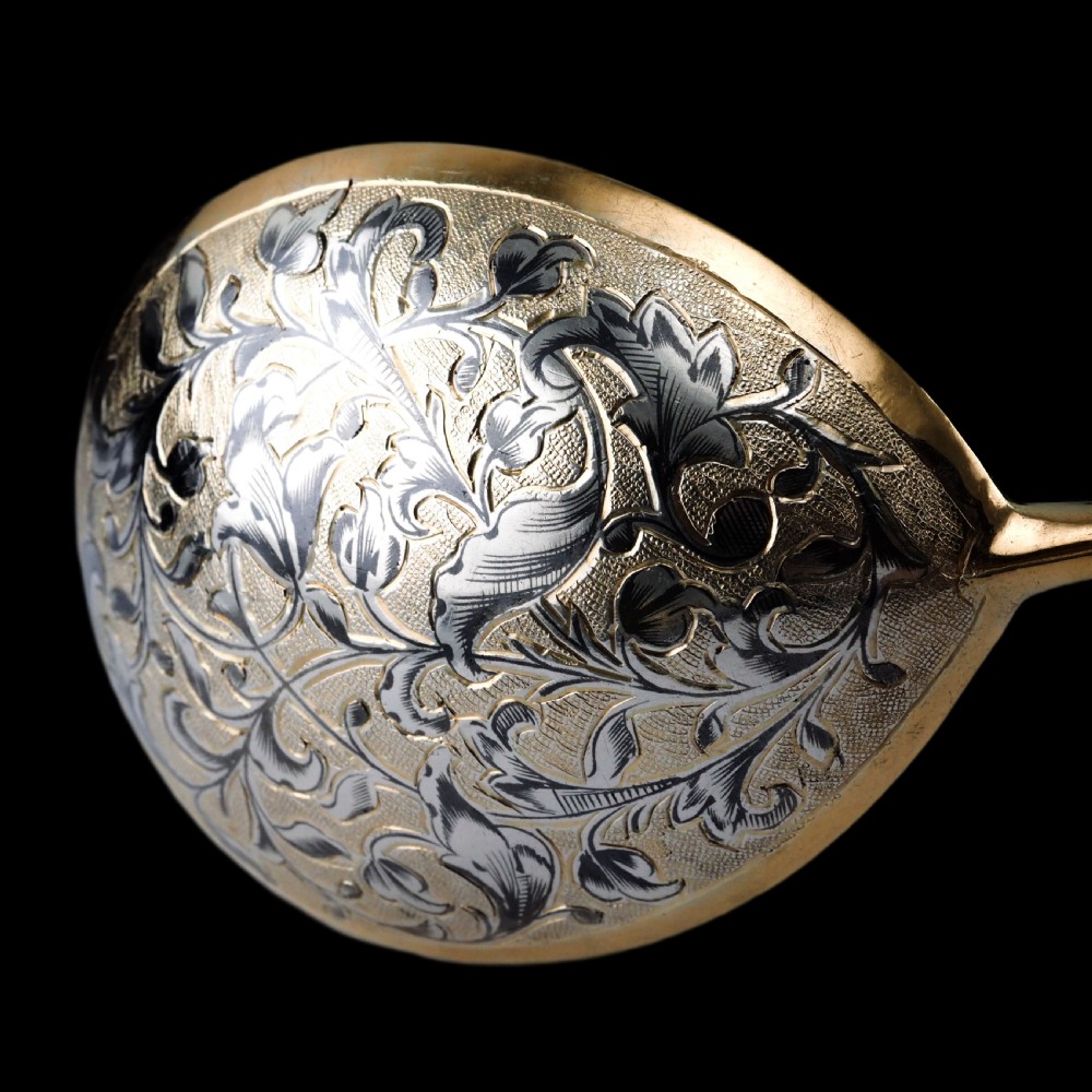 An antique Russian silver-gilt serving spoon featuring intricate black niello foliate engraving across the back of the oval bowl and a turned stem. View XVIII
