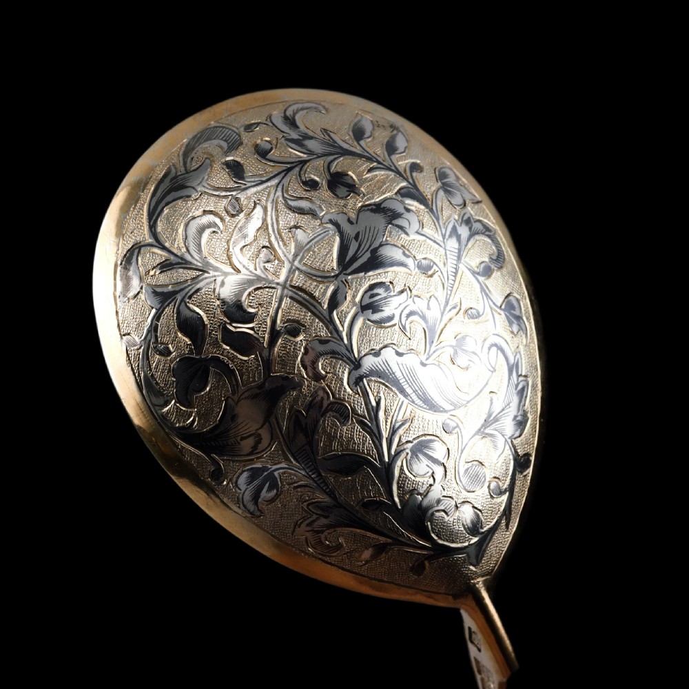 An antique Russian silver-gilt serving spoon featuring intricate black niello foliate engraving across the back of the oval bowl and a turned stem. View XX