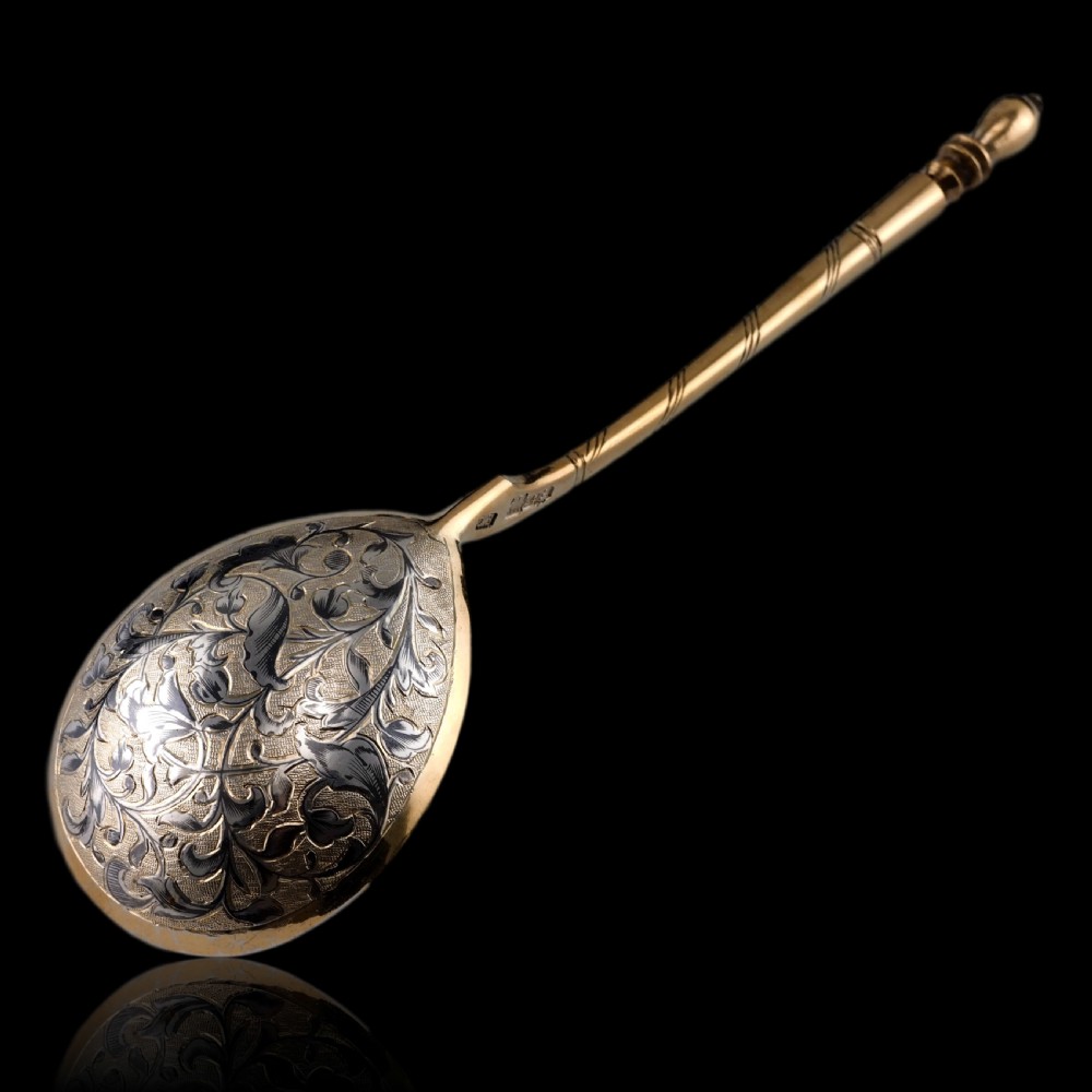 An antique Russian silver-gilt serving spoon featuring intricate black niello foliate engraving across the back of the oval bowl and a turned stem. View XXVI