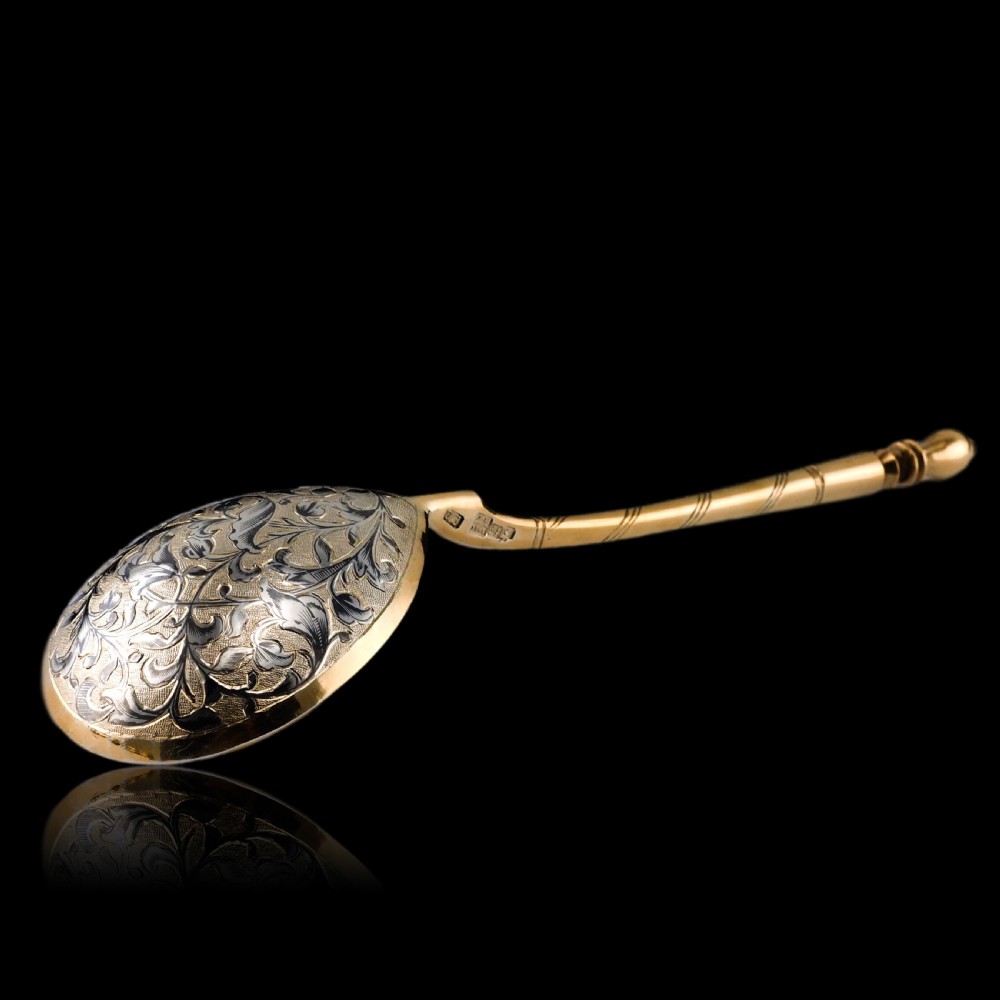 An antique Russian silver-gilt serving spoon featuring intricate black niello foliate engraving across the back of the oval bowl and a turned stem. View XXVII